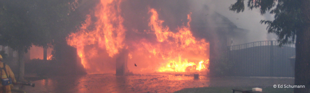 A wildfire burning a home with flames coming out of the garage.